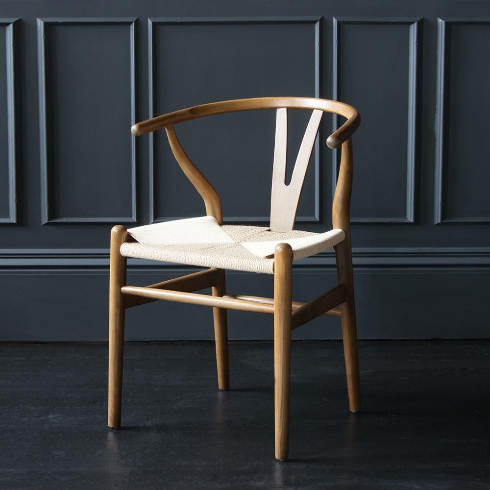 Hans J. Wegner - Chaise Wishbone en bois clair dans une pi&egrave;ce sombre.